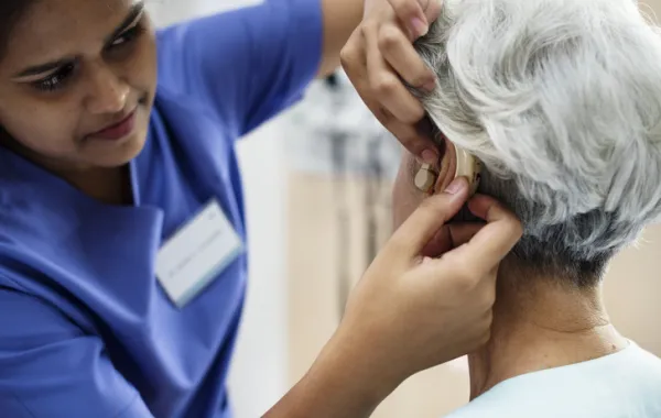 Foto de un sanitario ajustando al audífono a una señora