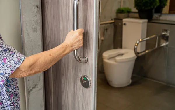 Foto del brazo de una persona mayor abriendo la puerta de un baño adaptado