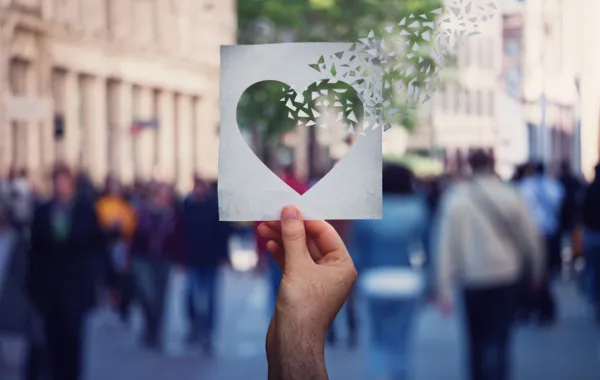 Foto de personas en la calle y una mano que sostiene un hoja con un corazon transparente