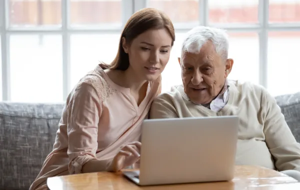 Foto de un señor mayor aprendiendo a usar un ordenador con una mujer joven