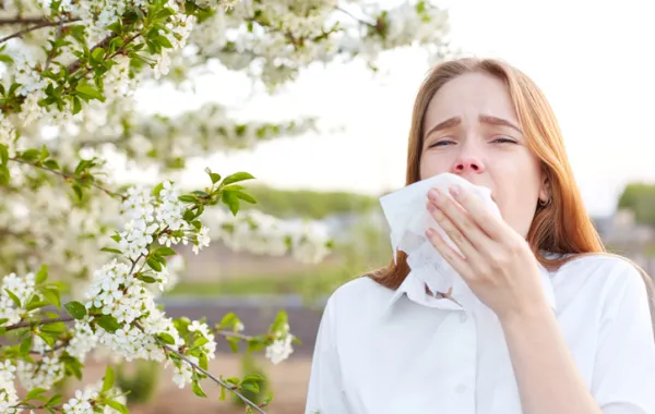 Foto de una mujer en un parque y con un pañuelo mientras estornuda