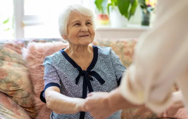 Foto de una señora mayor sentada en un sillón y dando las manos a una trabajadora social