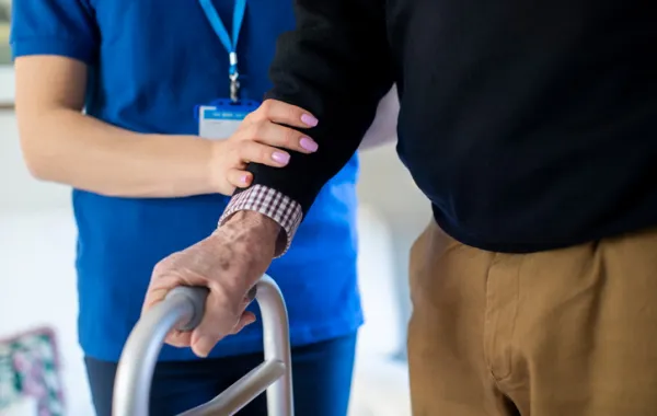 Foto de una persona mayor con discapacidad física agarrad por el brazo por un trabajador social