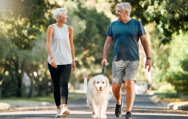 Foto de una pareja de personas adultas paseando por el parque con su perro