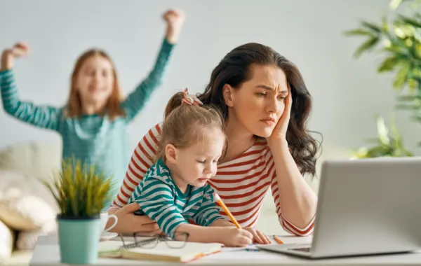Foto de una mujer trabajando en el ordenador mientras cuida a sus dos hijos