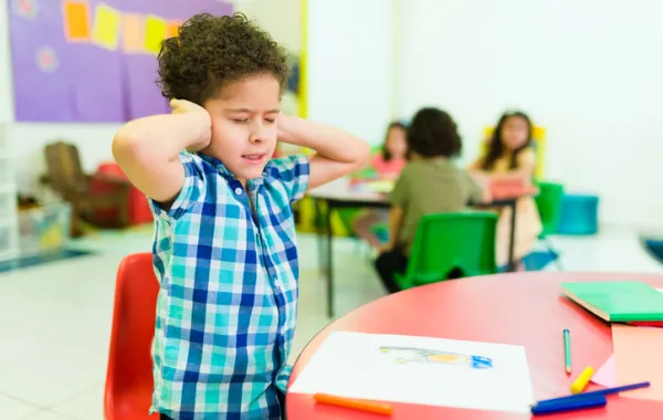 Foto de una clase con un niño pequeño que se tapa los oídos y cierra los ojos