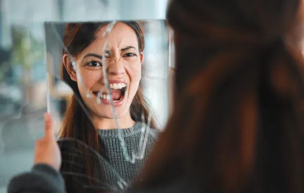 Foto de una mujer joven gritando frente a un espejo roto