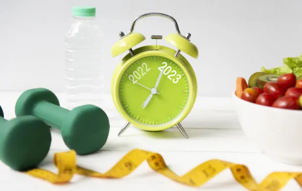 Foto de un reloj junto a una pesas de ejercicio, una cita métrica y una fruta