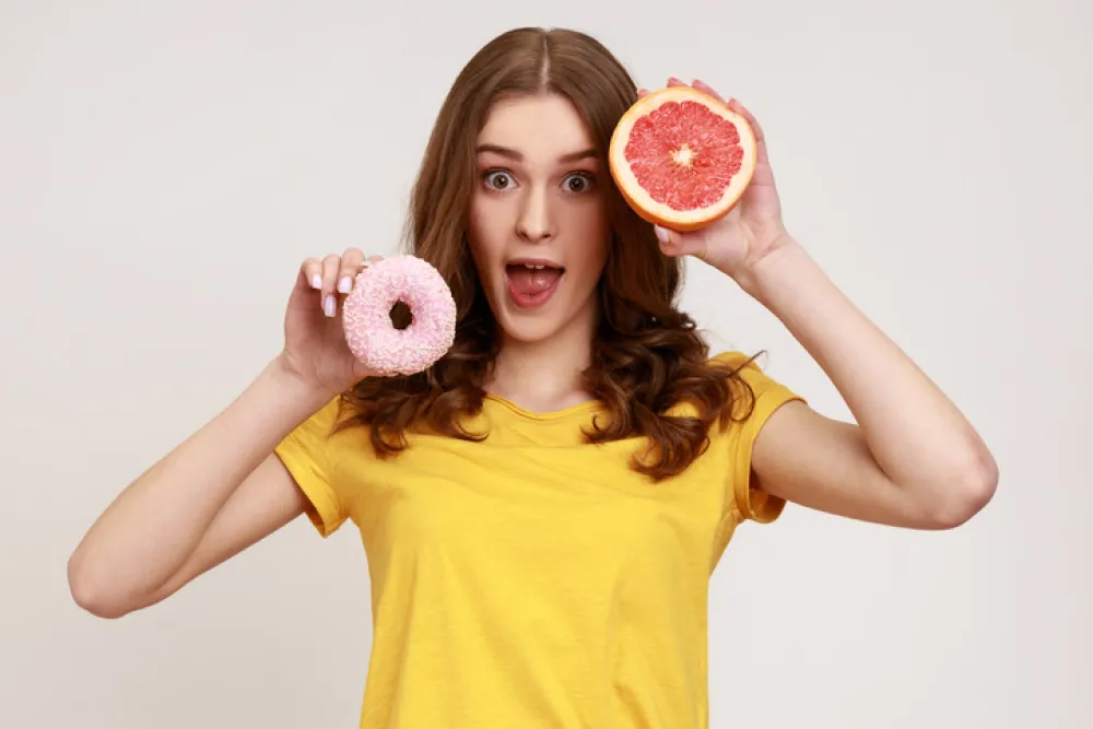 Foto de uma mujer que sostiene en una mano un donuts y en la otra un pomelo