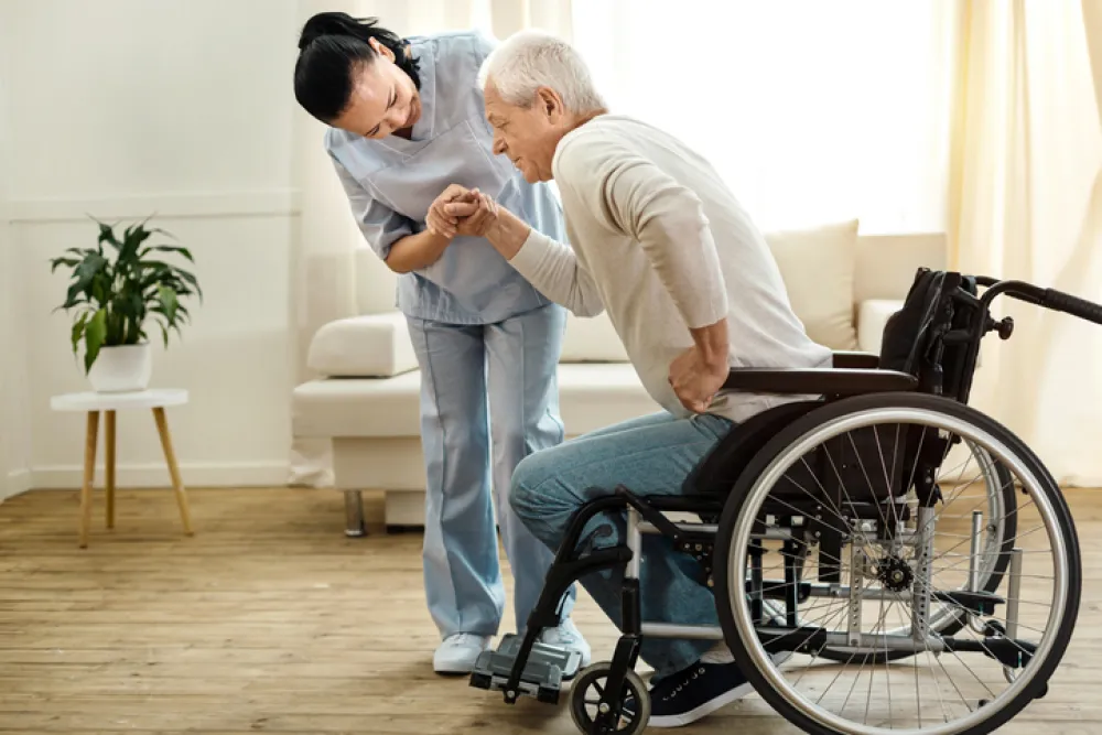 Foto de un señor que se levanta de luna silla de ruedas y es ayudado por una enfermera