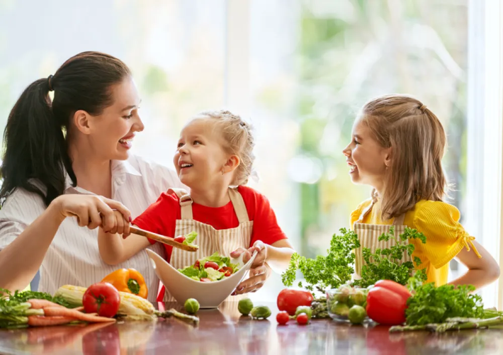 Foto de una madre con dos niños pequeñeos preparando una ensalada 