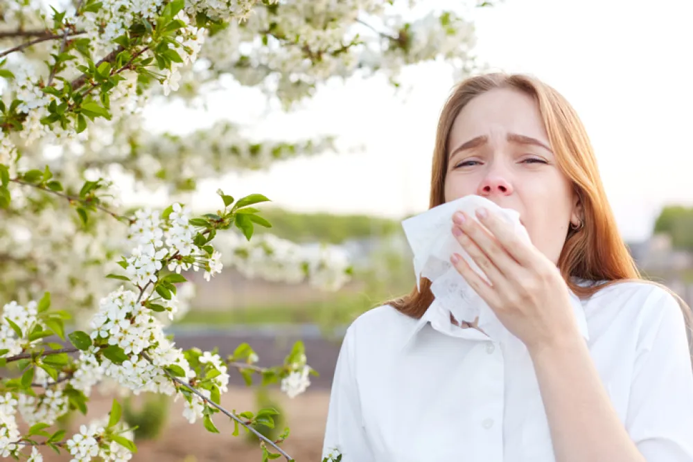 Foto de una mujer joven al lado de un árbol en flor y a punto de estornudar con un pañuelo preparado