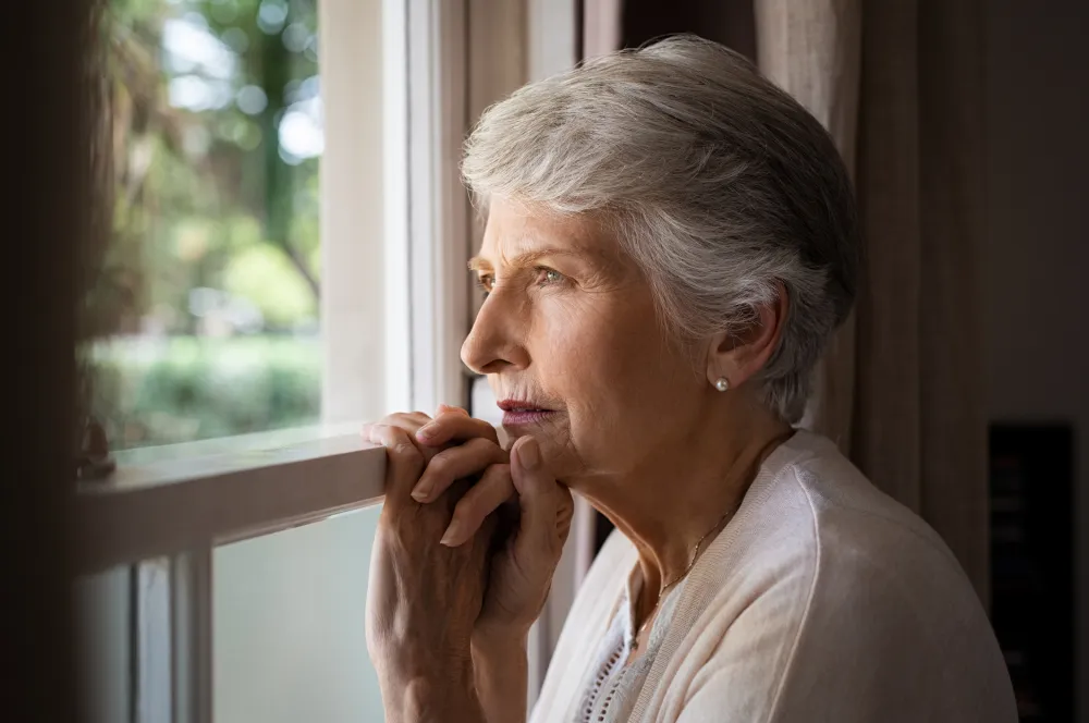 Foto de una señora mayor que mirando por la ventana con la mirada perdida