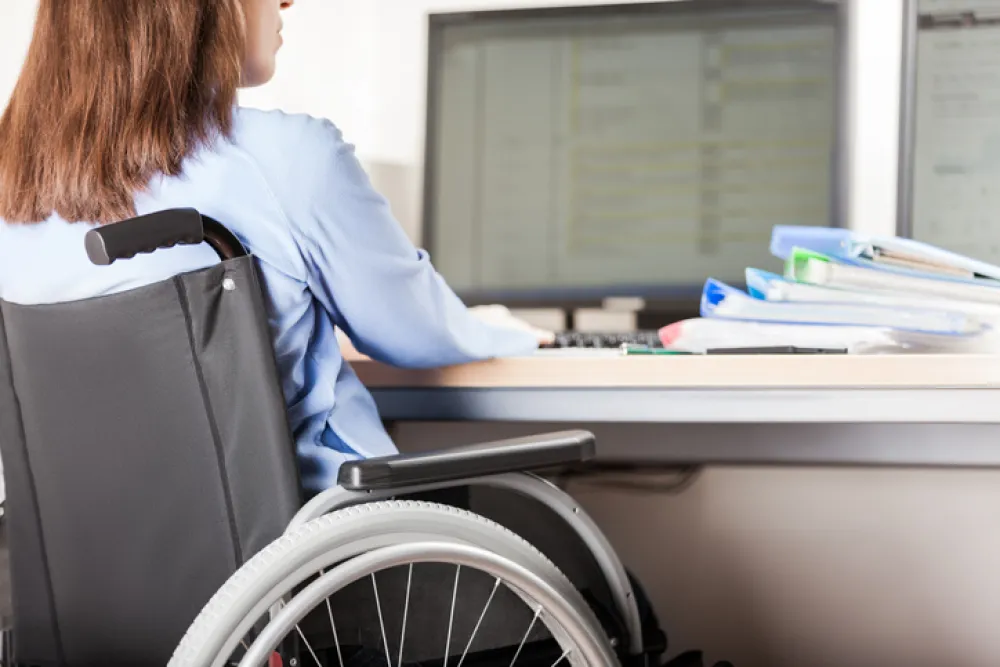 Foto de una mujer en silla de ruedas sentada en una mesa de oficina con ordenador