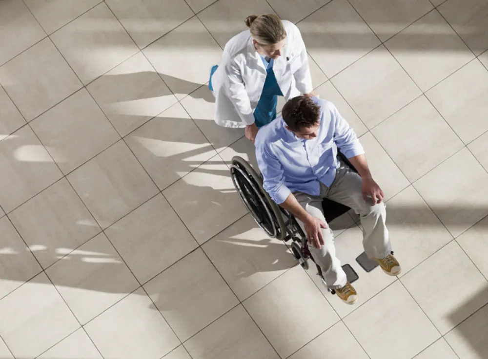 Foto de un señor en silla de ruedas acompañado por una enfermera