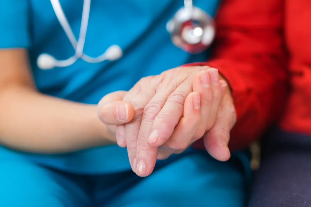 Foto de una mano de una persona anciana que es sostenida por la mano de un medico