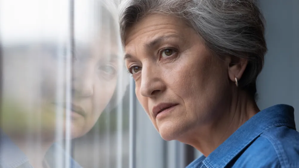 Foto de una señora adulta mirando por la ventana con cara triste