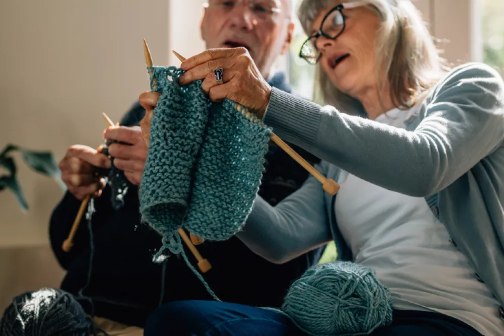 Foto de una señora mayor enseñando a tejer a otro señor mayor