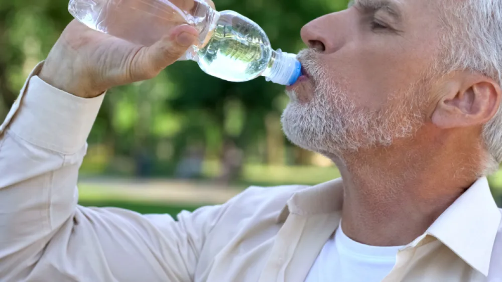 Foto de un señor adulto bebiendo agua de una botella