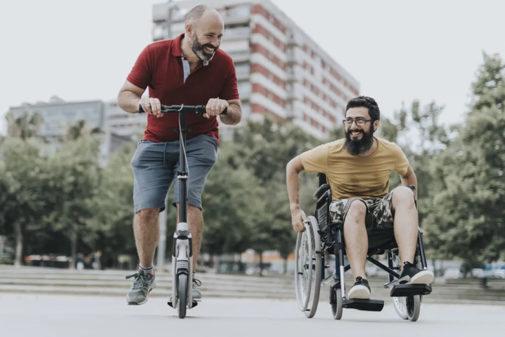 Foto de dos hombres uno en silla de ruedas y otro en patinete