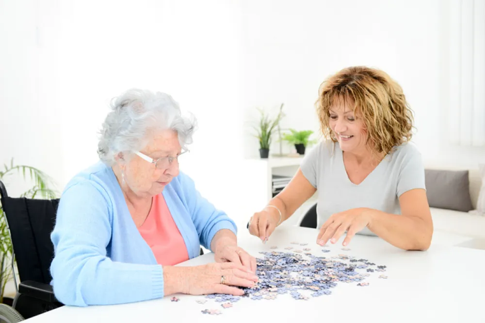 Foto de una señora mayor acompañada por una señora más joven haciendo un puzzle juntas