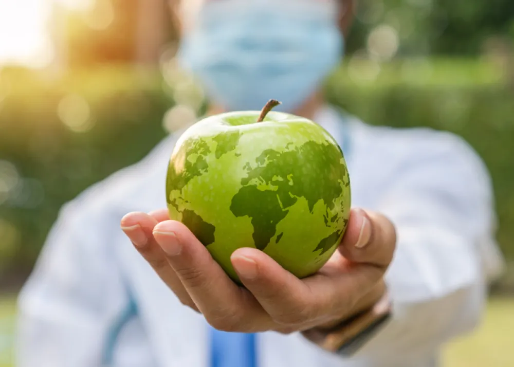 Foto de una persona sosteniendo una manzana con el dibujo del mundo impreso en la superficie de la manzana