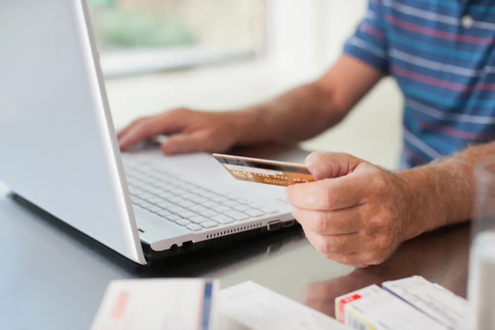 Foto de una persona delante de un ordenador realizando una compra online y sosteniendo una tarjeta de crédito en la mano