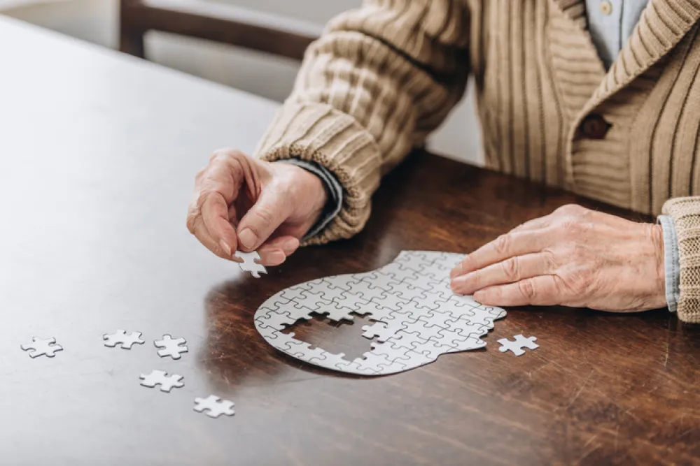 Foto de las manos de una persona mayor haciendo un puzzle con la figura de una cabeza