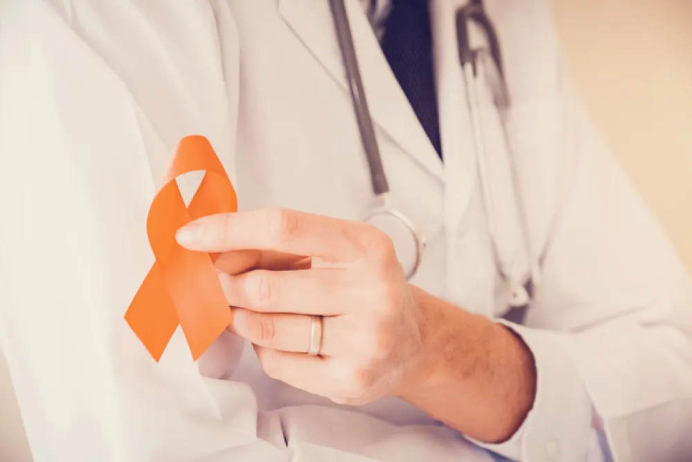 Foto de un médico que sostiene en la mano un lazo naranja símbolo de esclerosis multiple