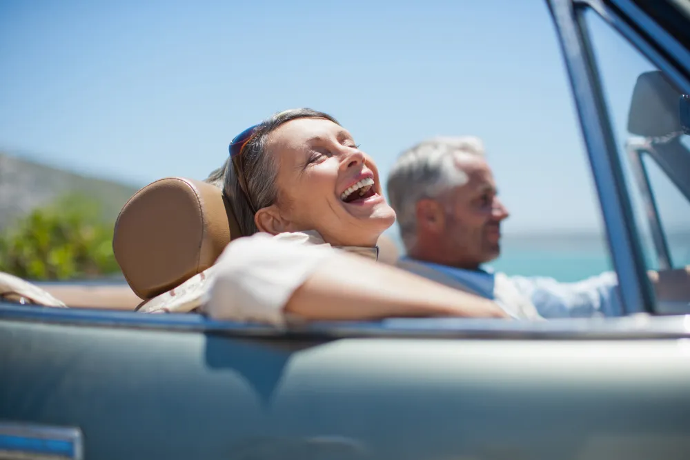 Foto de una pareja de personas maduras que sonrien mientras van en un coche descapotable