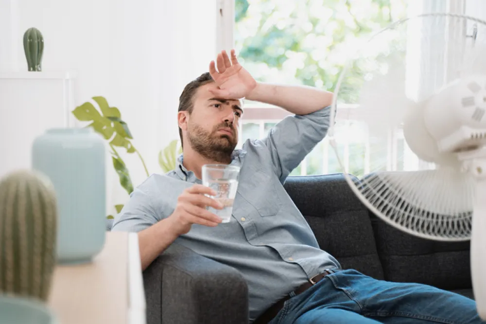 Foto de un señor sentado en un sillón con sintomas de sofoco por calor y un vaso de agua en la mano