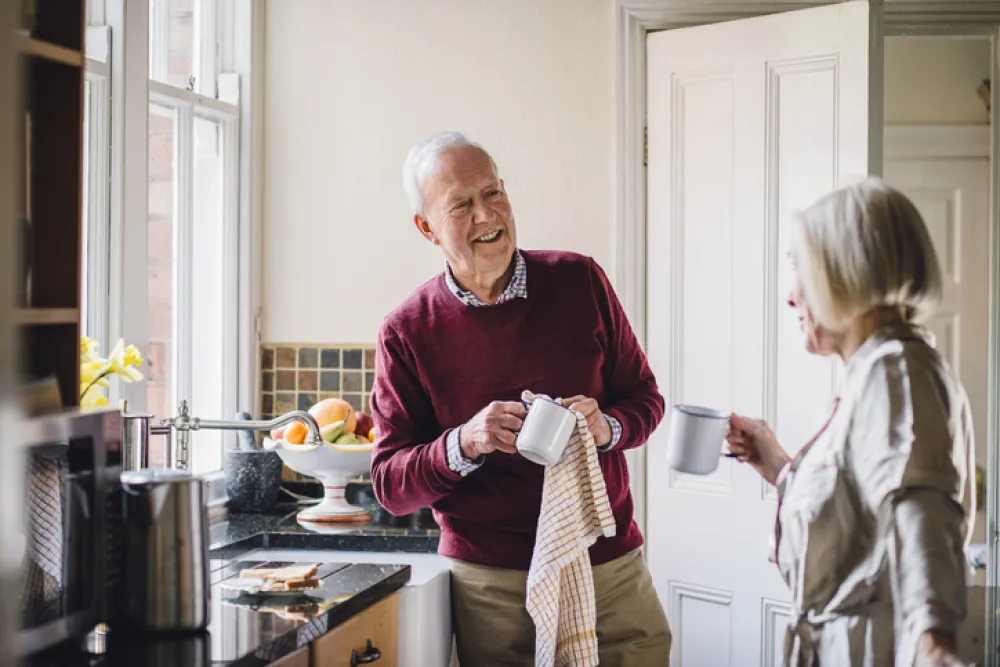 Foto de dos personas mayores charlando en una cocina mientras limpian los platos