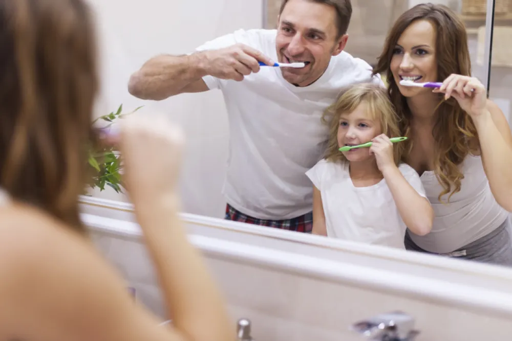 Foto de una familia lavándose los dientes mientras se miran en un espejo