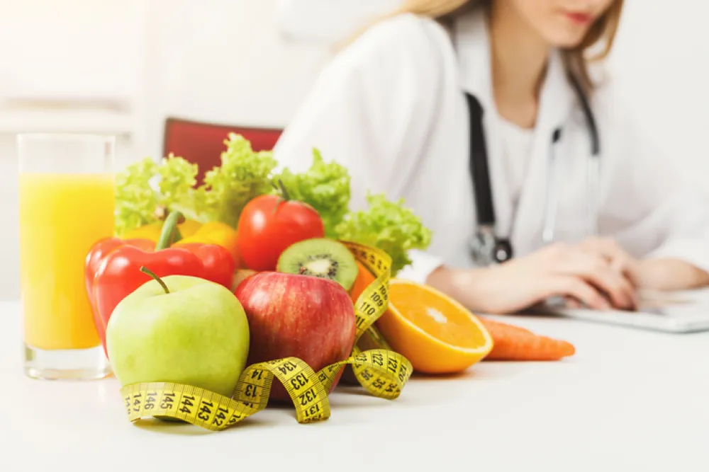 Foto de una mesa llena de frutas y una doctora sentada al lado