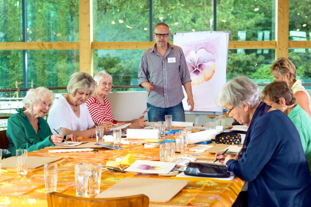 Foto de varias personas mayores pintando mientras un profesor les enseña un dibujo