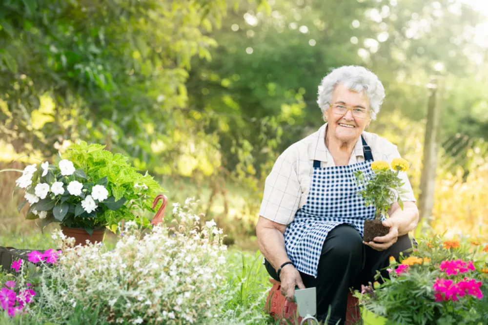 Foto de una mujer mayor en un jardín y colocando macetas de flores