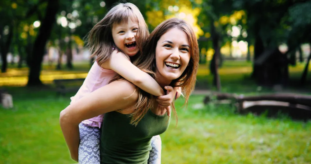 Foto de madre joven con su hija con síndrome de down sonriendo felices