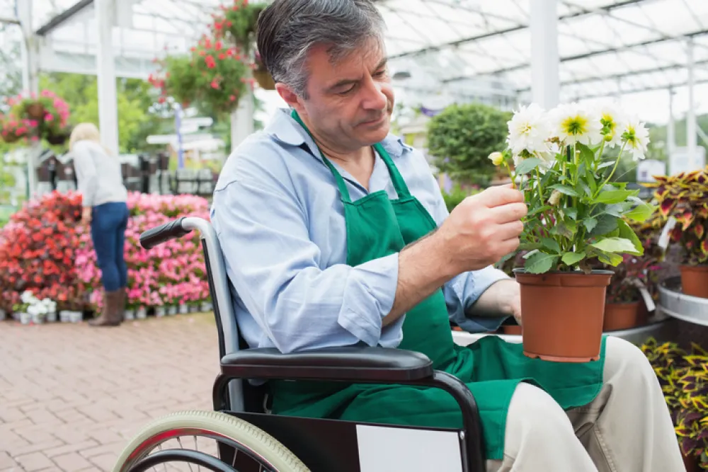 Foto hombre en silla de ruedas arreglando una maceta con un planta