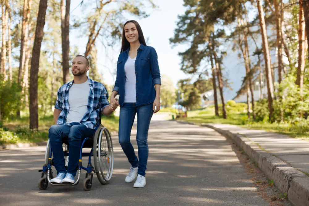 Foto de un joven en silla de ruedas acompañado por una mujer joven mientras pasean