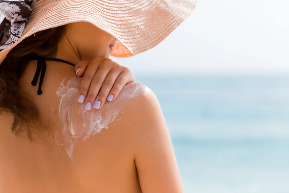 Foto de una mujer que se está echando crema solar por la  espalda y hombros