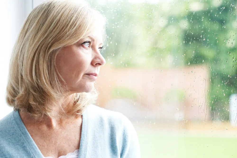 Foto mujer mediana edad mirando con tristeza a través de una ventana con gotas de lluvia