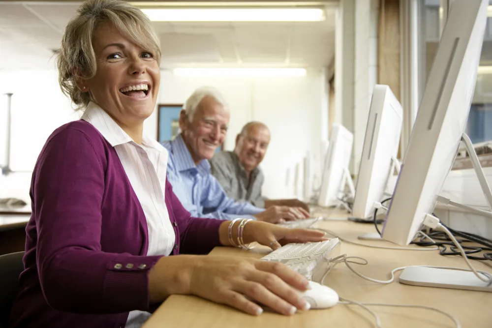 Foto de personas de 60 años delante de un ordenador y sonriendo