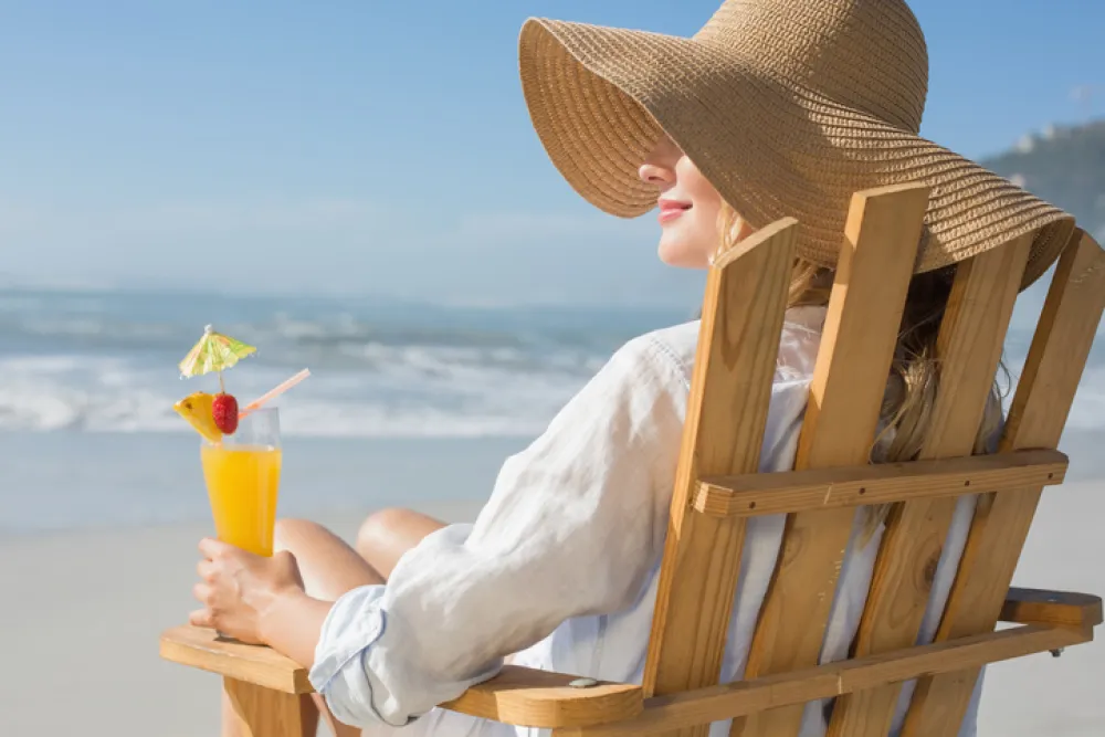 Foto de mujer frente al mar sentada, con un gorro y una bebida