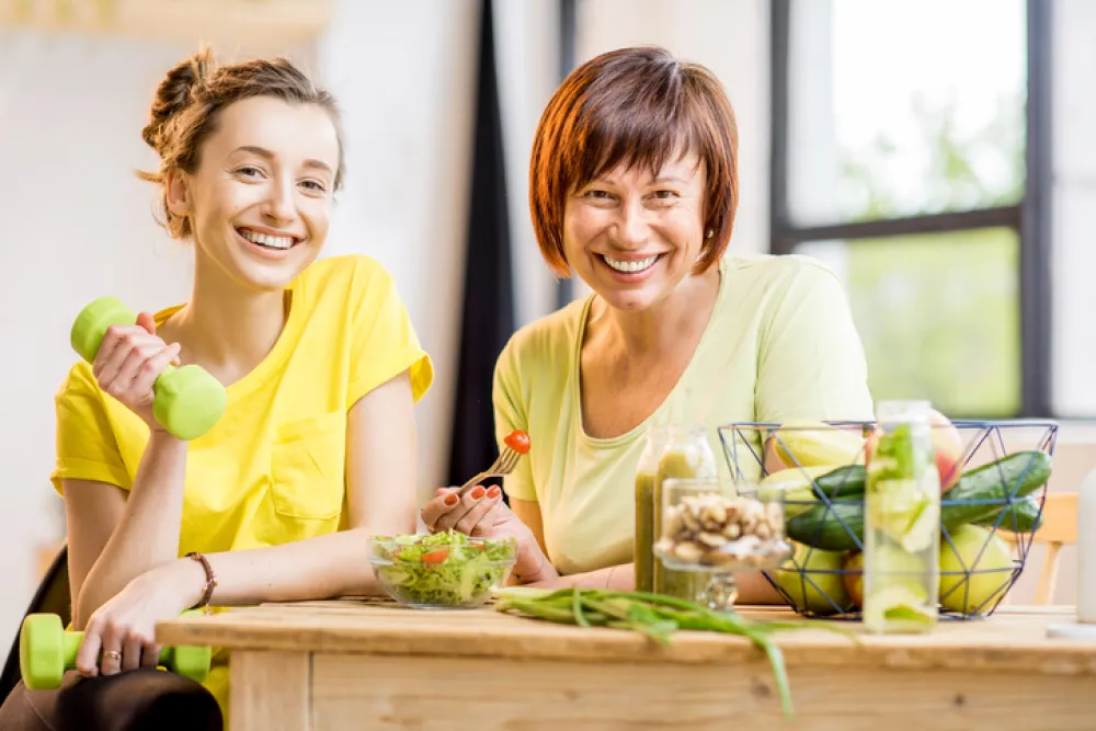 Una madre y una hija sonríen delante de una mesa con verduras