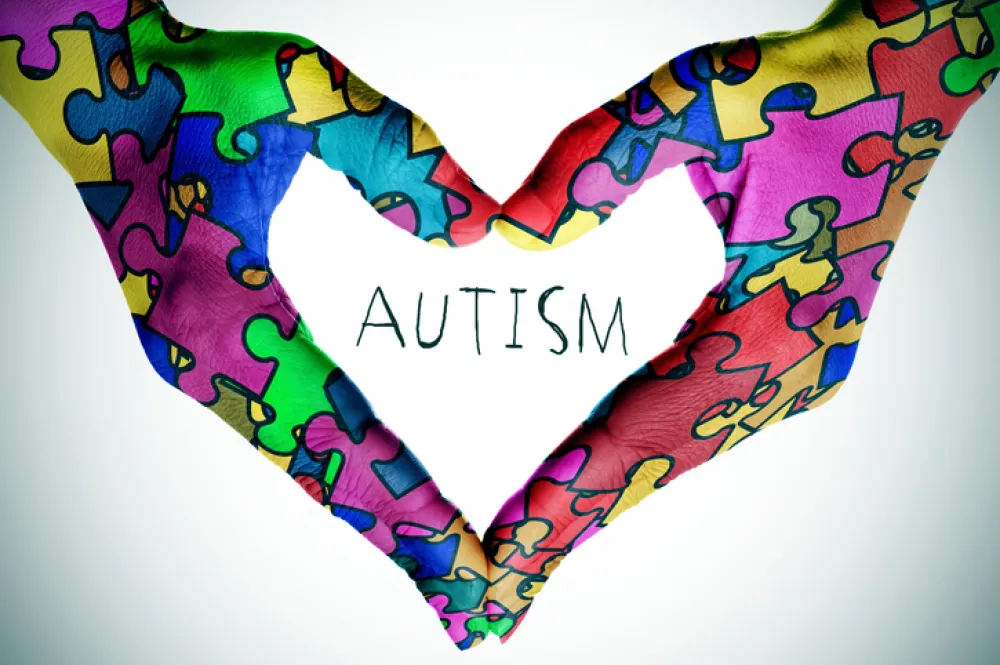 Foto con un cartel de unas manos formando un corazon y la palabra autismo en el centro