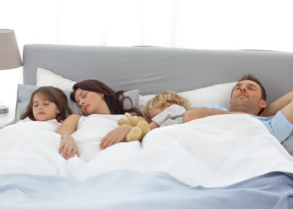 Foto de una familia con dos niños pequeños que duermen en una cama