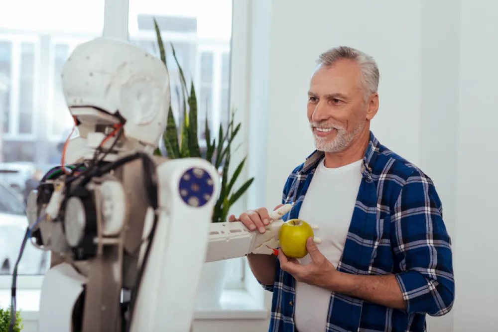 Foto de hombre maduro acompañado de un robot que le ofrece una fruta