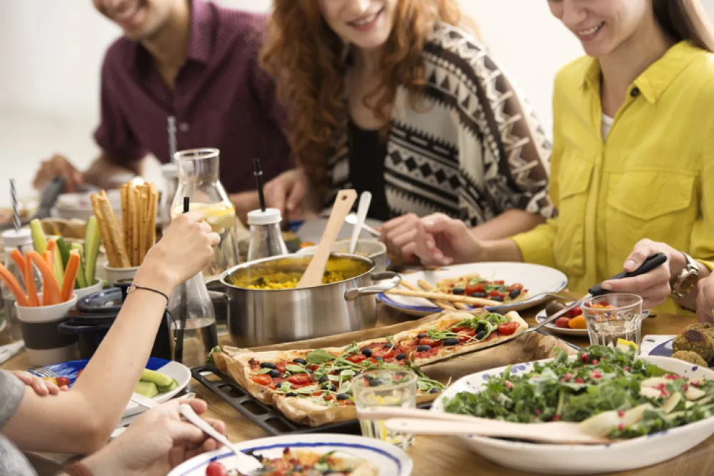 Foto de una mesa llena de comida vegetariana y rodeada de personas sonrientes