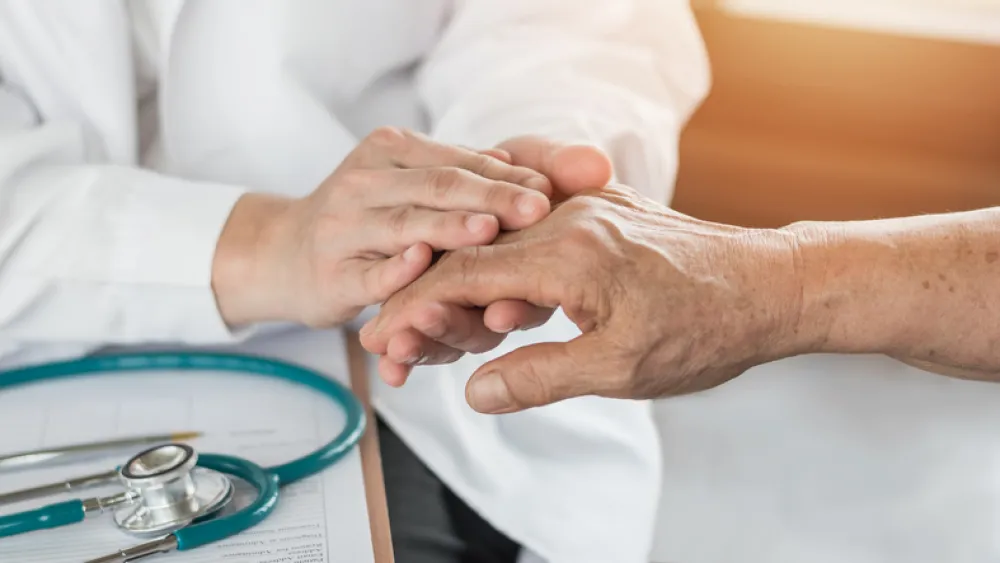 Foto de un mano de una persona mayor que es recogida por las dos manos de un medico