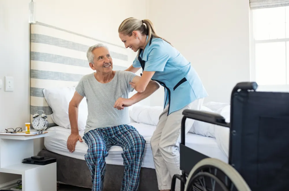 Foto de un señor mayor en silla de ruedas ayudado por una enfermera